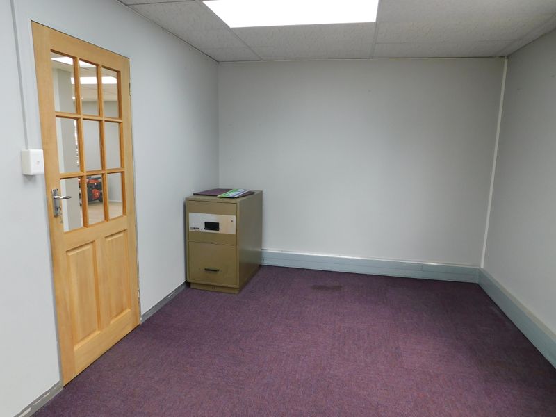 A vacant office space featuring a timber-framed glass door, suspended ceiling with recessed lighting, and purple carpeting.