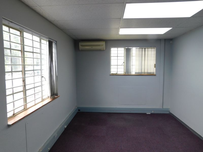 A vacant office space featuring a suspended ceiling, recessed lighting, split-system air conditioning, and security bars on the windows.