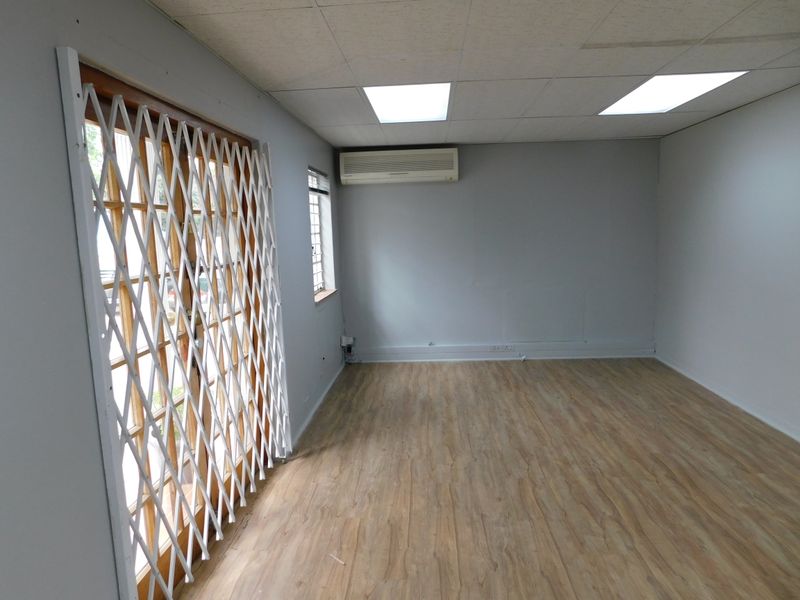 A vacant office space featuring laminate flooring, a split-system air conditioner, recessed lighting, and a security gate over the glass door.