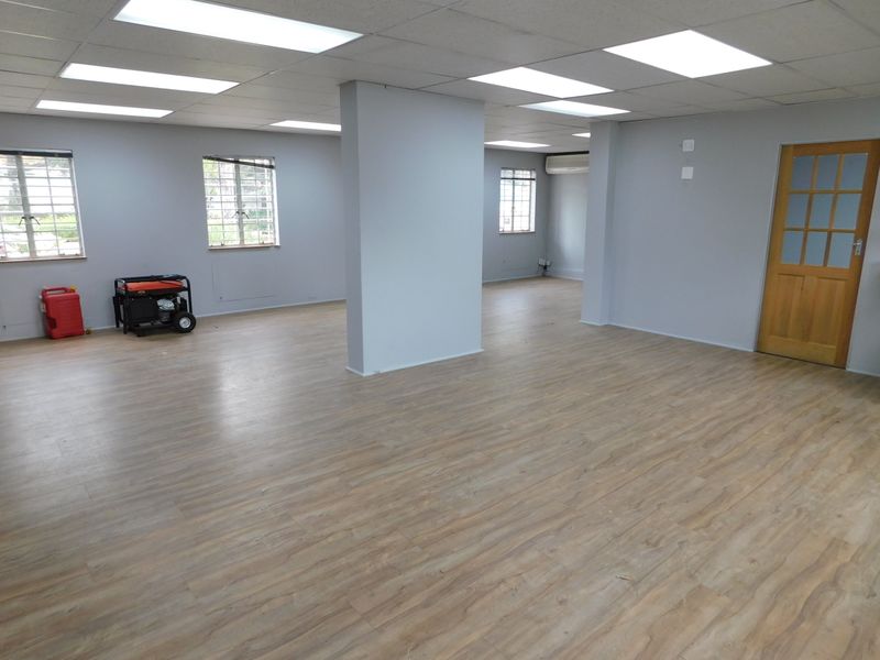 Spacious open-plan office area featuring laminate flooring, recessed ceiling lighting, air conditioning, and large windows with security bars.
