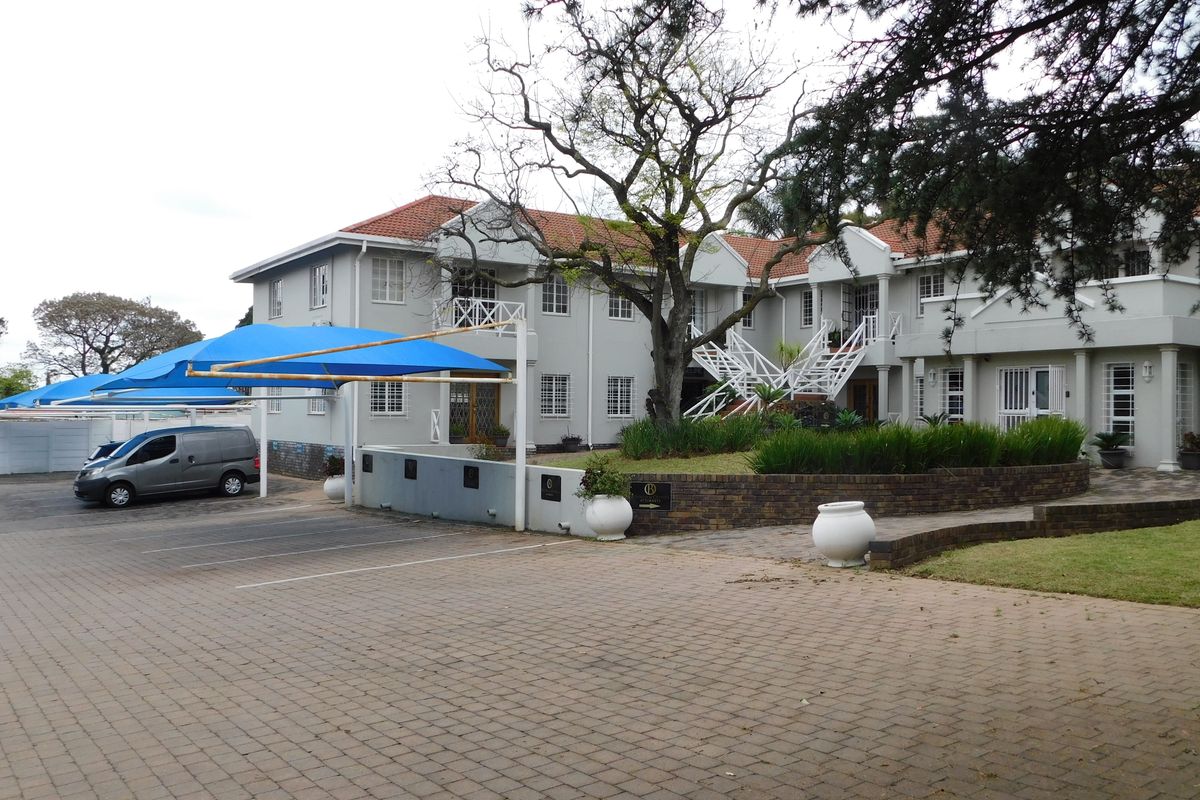 Front view of a multi-story office building featuring a paved parking area with shade cloth carports, landscaped gardens, and an external staircase.