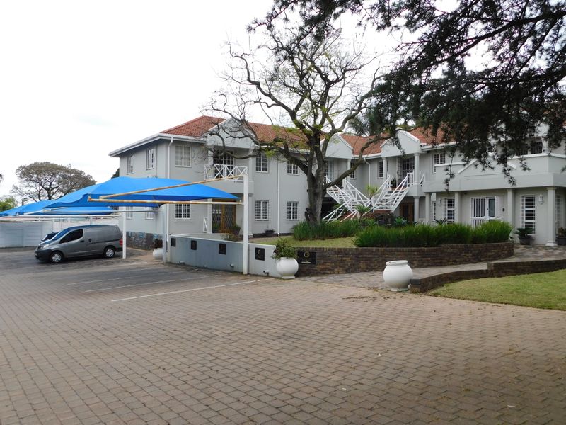 Front view of a multi-story office building featuring a paved parking area with shade cloth carports, landscaped gardens, and an external staircase.