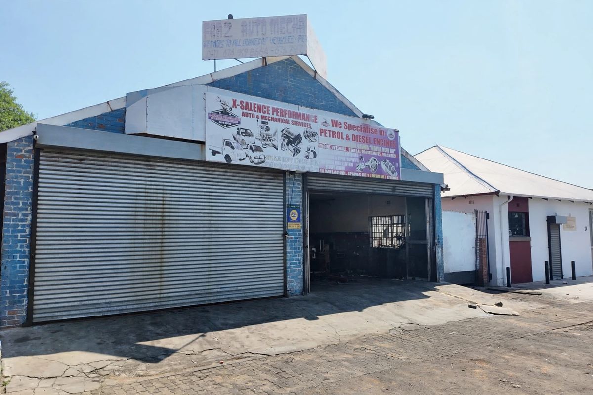Front exterior view of a commercial automotive workshop featuring a roller shutter door, brick facade, and prominent business signage.