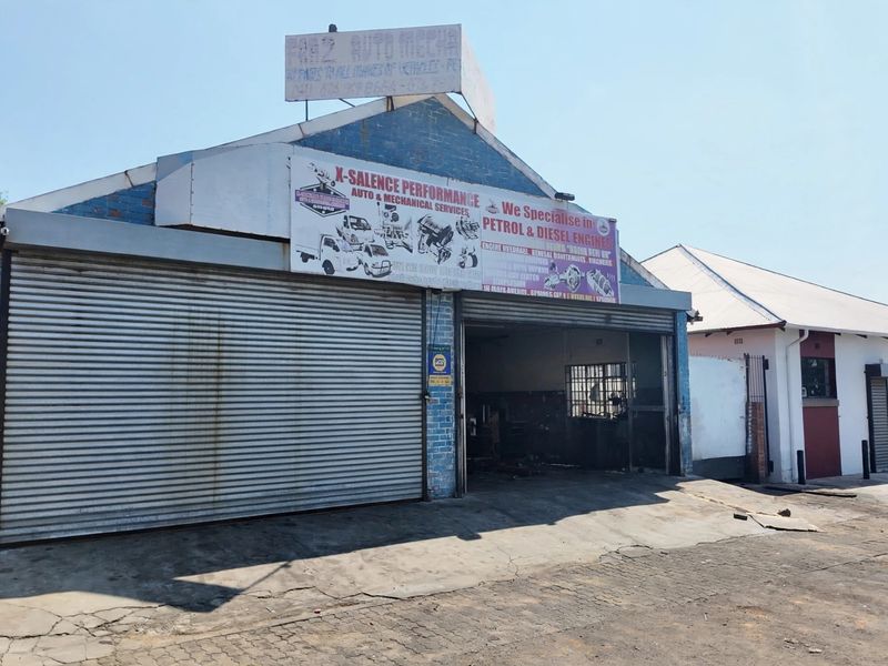 Front exterior view of a commercial automotive workshop featuring a roller shutter door, brick facade, and prominent business signage.