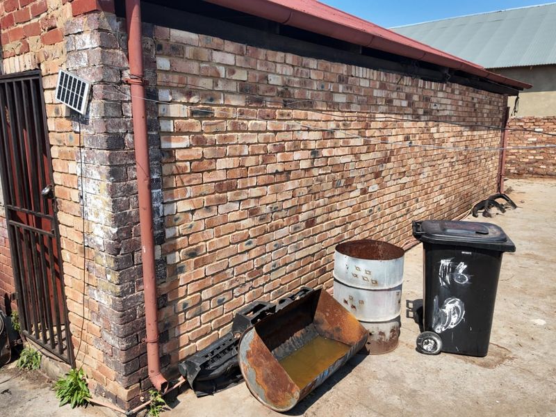 Rear exterior view of a brick building featuring a metal security gate, downpipe, and concrete paved area.