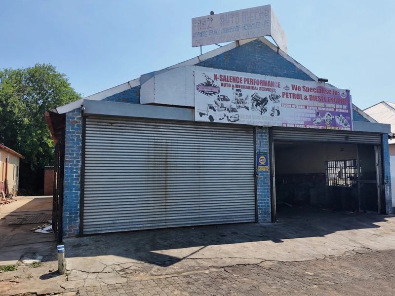 Front view of a commercial workshop featuring a roller shutter door, brick facade, and prominent business signage on a concrete driveway.