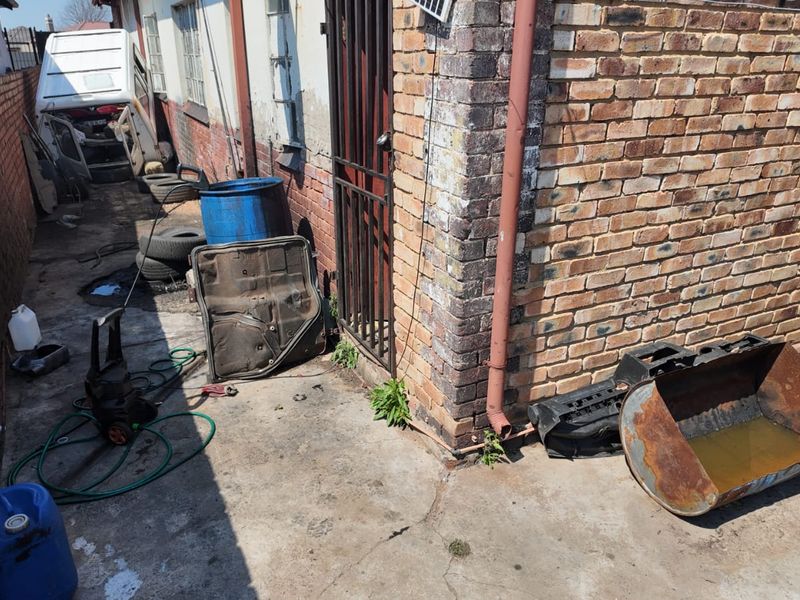 A narrow rear exterior service area featuring brick boundary walls, concrete paving, and a metal security gate access point.