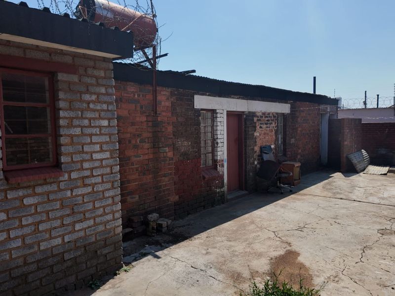 Rear exterior view of a brick building featuring a concrete paved yard, solar water heating system, and perimeter security fencing.