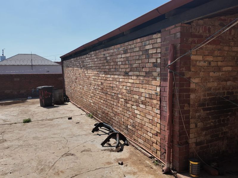 Rear exterior area featuring a long face brick wall, concrete paving, and perimeter walling with security razor wire.