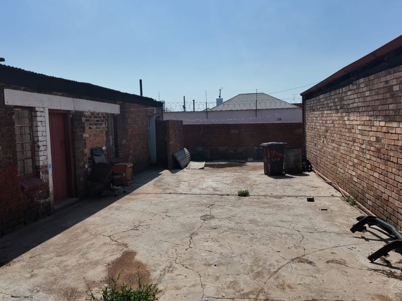 A rear exterior courtyard area featuring exposed brick walls and cracked concrete paving, enclosed by security fencing.