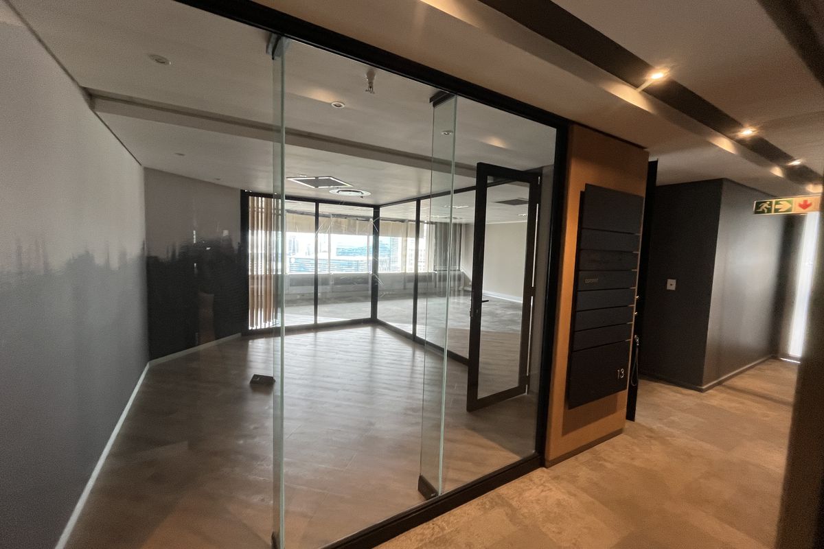 A modern, vacant office space featuring glass partition walls, recessed lighting, and high-quality laminate flooring, offering a professional and bright work environment.