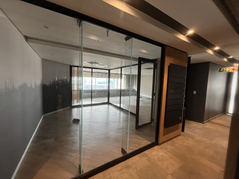 A modern, vacant office space featuring glass partition walls, recessed lighting, and high-quality laminate flooring, offering a professional and bright work environment.