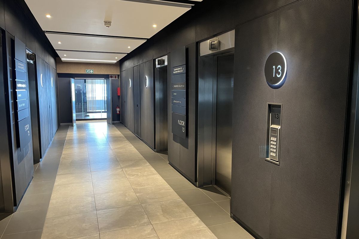 Modern office building elevator lobby featuring sleek metal wall paneling, tiled flooring, and recessed ceiling lighting on the 13th floor.