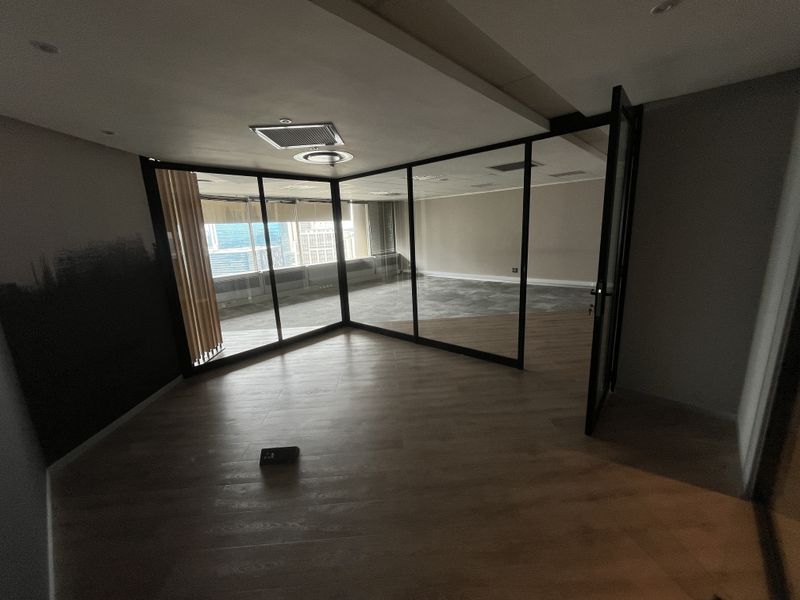 A modern, empty office space featuring glass partition walls, recessed ceiling lighting, and wood-look flooring, offering a clean and professional environment.
