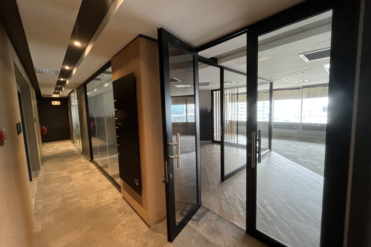 Modern office space featuring glass partitions, black metal framing, recessed lighting, and carpeted flooring, offering a professional and open work environment.