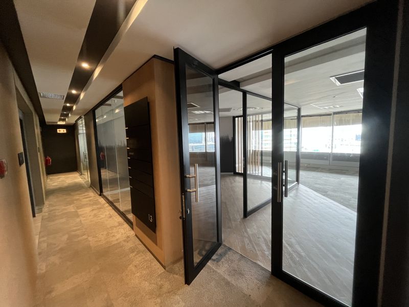 Modern office space featuring glass partitions, black metal framing, recessed lighting, and carpeted flooring, offering a professional and open work environment.
