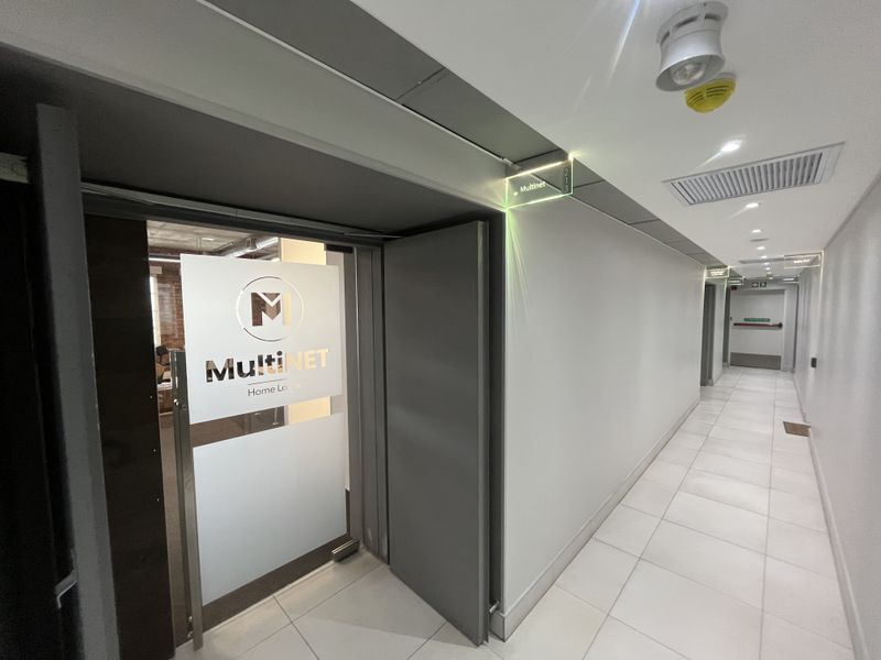A clean, modern office hallway featuring tiled flooring, recessed lighting, and clear directional signage leading to the office entrance.