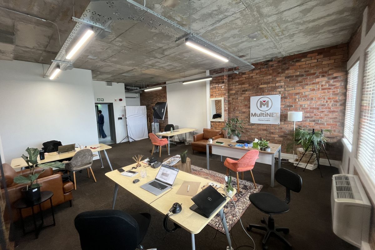 Spacious open-plan office featuring an industrial aesthetic with exposed concrete ceilings, brick feature walls, and modern linear lighting.