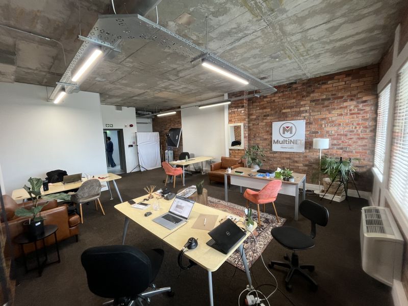 Spacious open-plan office featuring an industrial aesthetic with exposed concrete ceilings, brick feature walls, and modern linear lighting.
