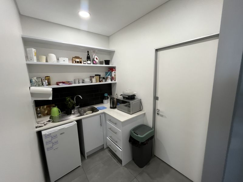 A compact, modern scullery or kitchenette area featuring built-in cabinetry, a stainless steel sink, black subway tile backsplash, and open shelving.