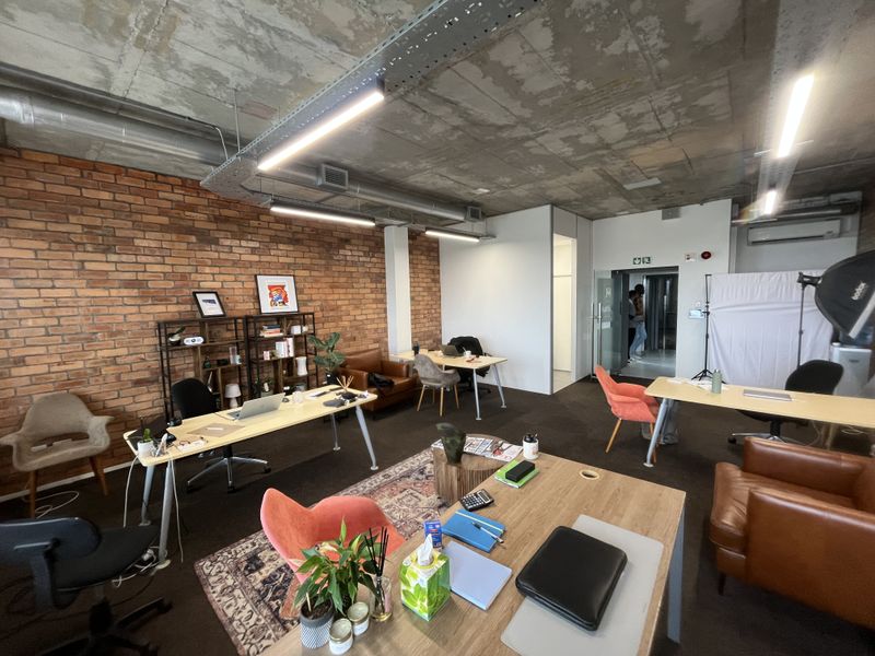 Modern open-plan office space featuring an exposed concrete ceiling, industrial-style cable trays, and a prominent exposed brick feature wall.