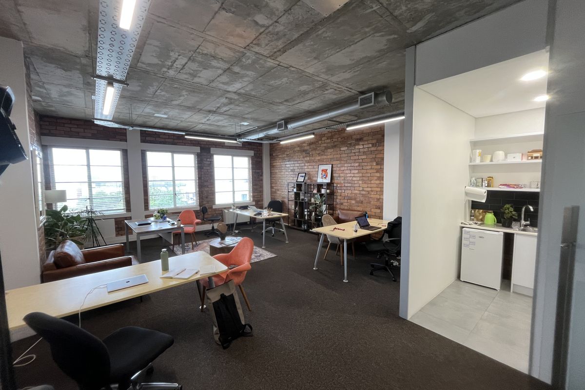 Modern open-plan office space featuring exposed concrete ceilings, brick feature walls, and a convenient integrated kitchenette area.