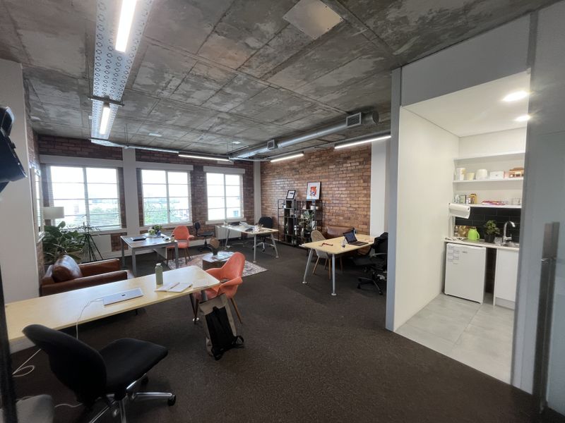 Modern open-plan office space featuring exposed concrete ceilings, brick feature walls, and a convenient integrated kitchenette area.