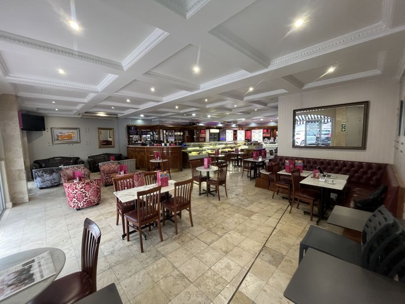 Spacious open-plan commercial dining area featuring a coffered ceiling, recessed lighting, stone tile flooring, and a built-in service counter with display cabinets.