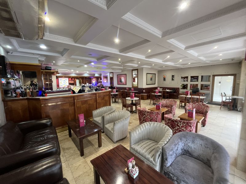 Spacious open-plan commercial lounge area featuring a built-in bar, coffered ceilings with recessed lighting, and tiled flooring throughout.