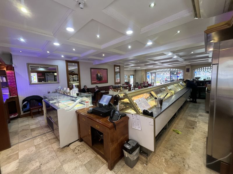 Spacious commercial interior featuring a coffered ceiling, recessed lighting, stone tile flooring, and extensive built-in service and display counters for food service.