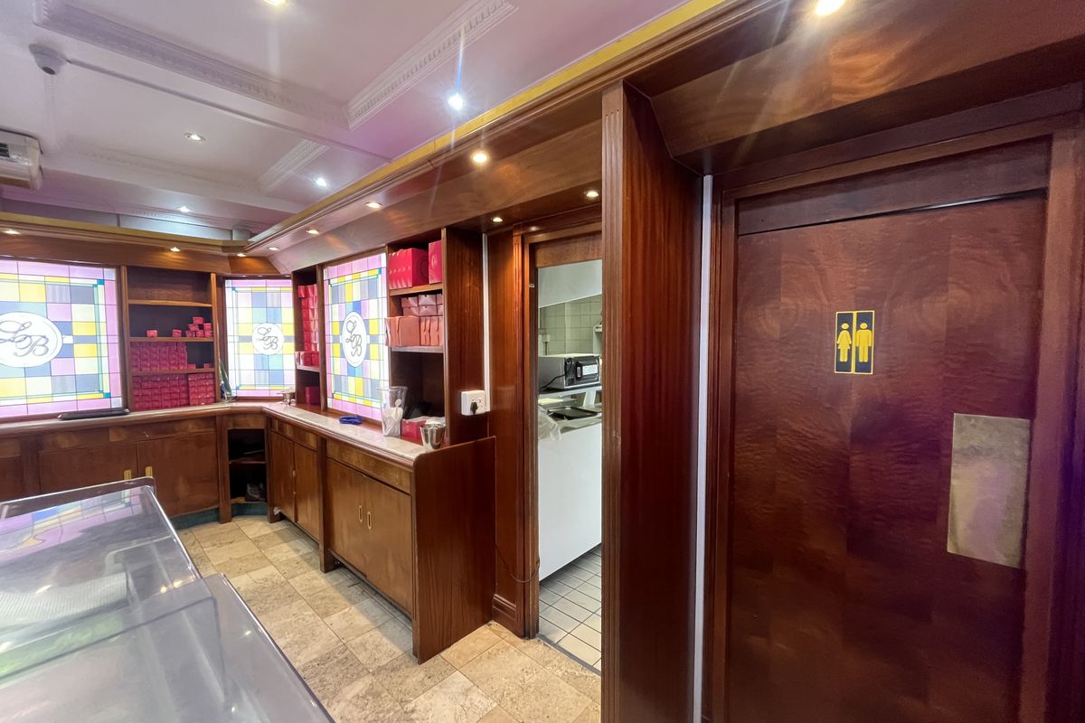Commercial kitchen area featuring custom built-in wooden cabinetry, decorative stained glass accents, recessed lighting, and tiled flooring with access to a restroom.