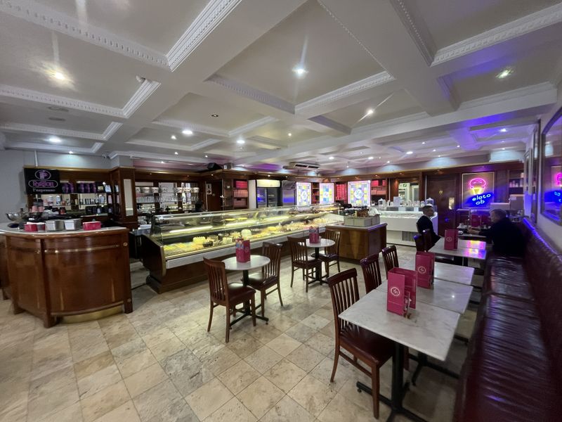 Spacious commercial cafe interior featuring a coffered ceiling, stone tile flooring, and a large built-in display counter with integrated refrigeration.