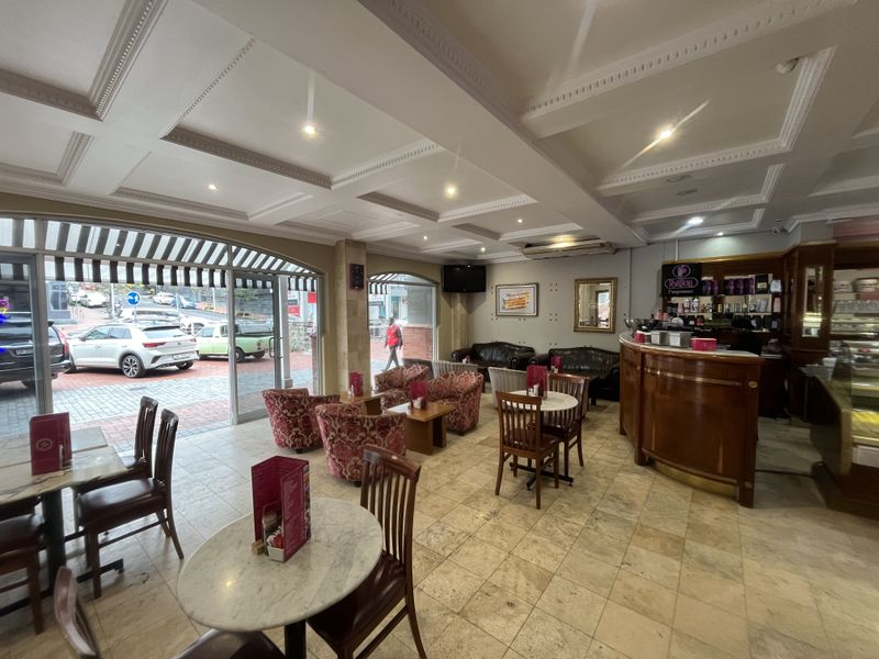 Spacious open-plan cafe interior featuring stone tile flooring, a coffered ceiling with recessed lighting, and a prominent built-in service counter with street-facing glass frontage.