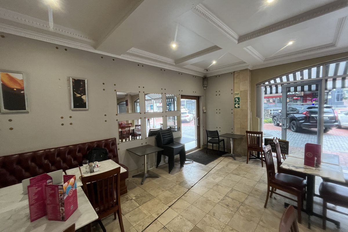 Interior view of a commercial dining space featuring tiled flooring, recessed ceiling lighting, and large glass entrance doors with street access.