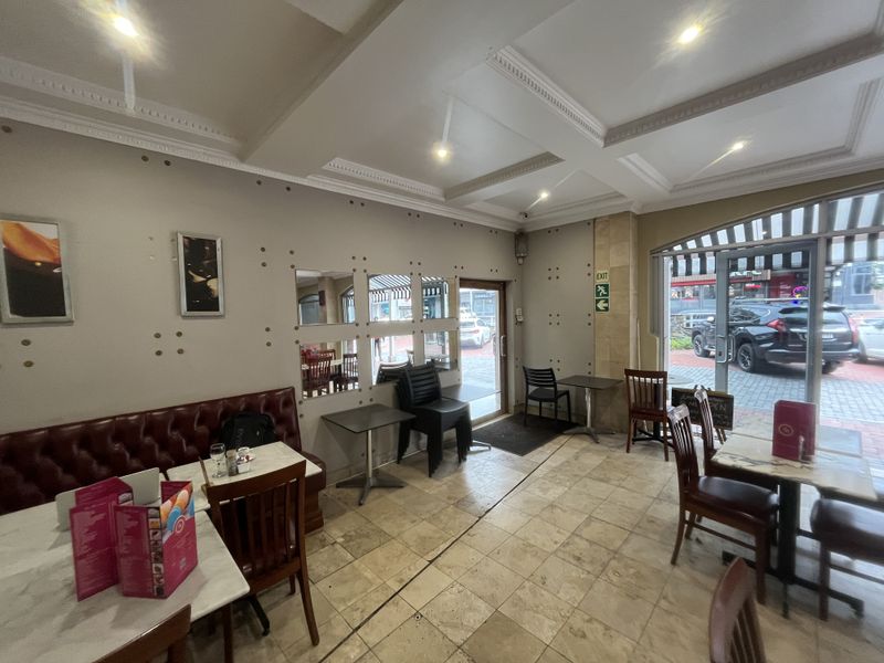 Interior view of a commercial dining space featuring tiled flooring, recessed ceiling lighting, and large glass entrance doors with street access.