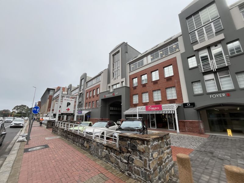 Front exterior view of Sovereign Quay commercial building featuring brick and grey facade, stone retaining wall, and ground-level retail access.