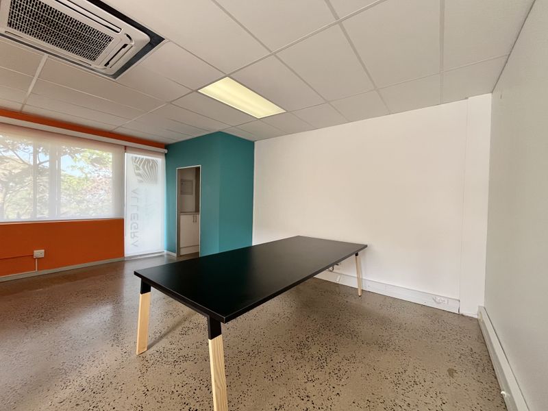 A bright, modern office space featuring polished concrete floors, a suspended ceiling with integrated air conditioning, and vibrant accent walls.