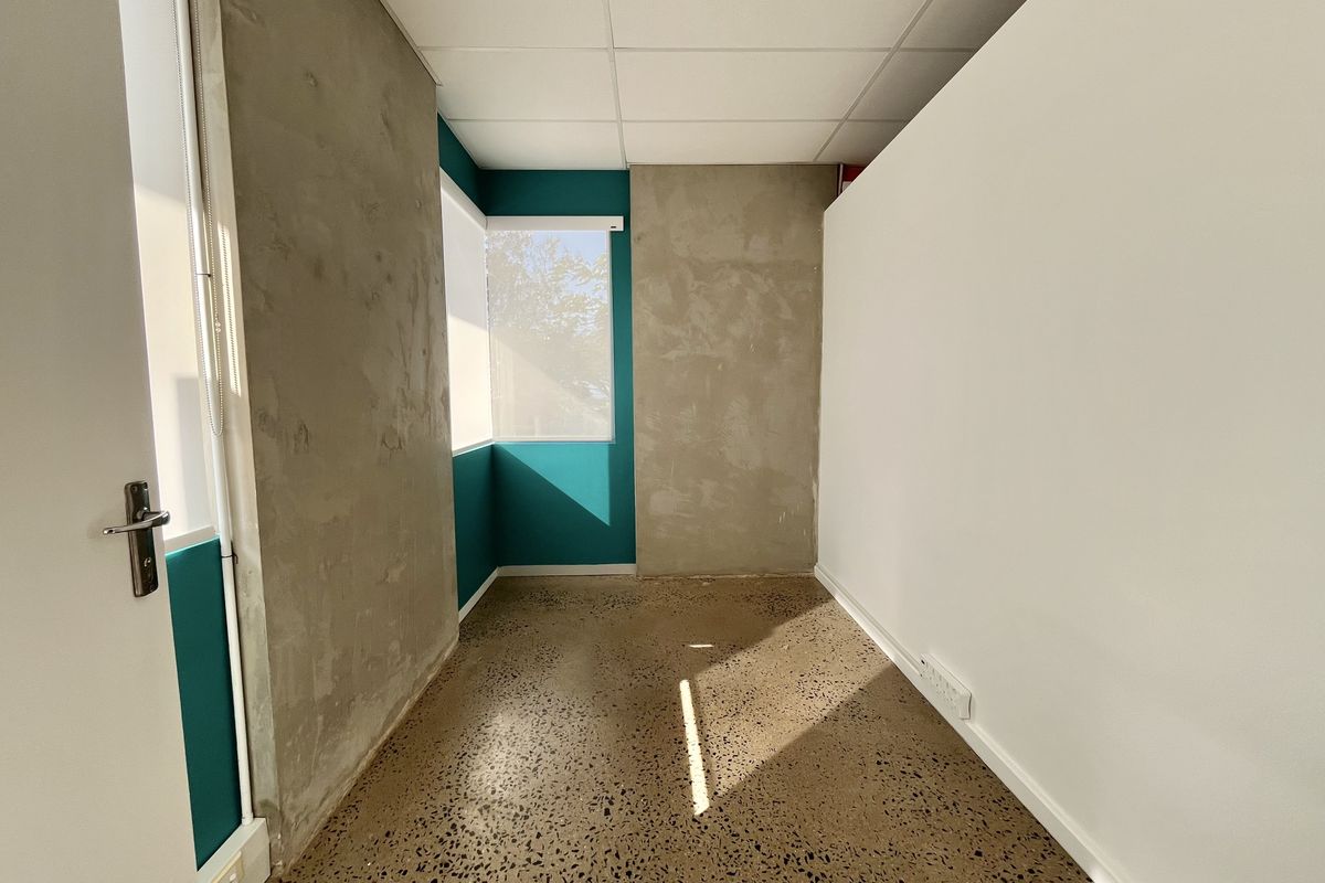 An empty office space featuring polished concrete flooring, suspended ceiling tiles, and unfinished concrete wall accents, offering a modern industrial aesthetic.