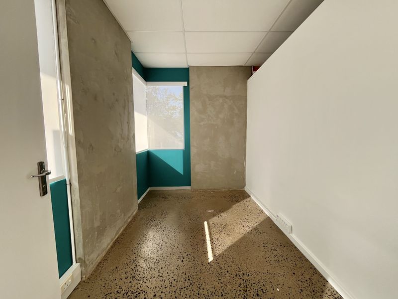An empty office space featuring polished concrete flooring, suspended ceiling tiles, and unfinished concrete wall accents, offering a modern industrial aesthetic.