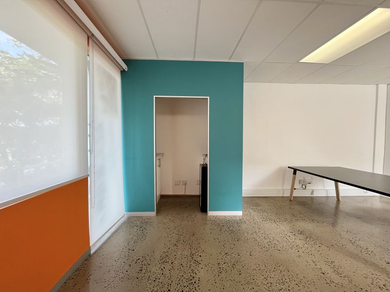 Modern office space featuring polished concrete flooring, a suspended ceiling with recessed lighting, and a dedicated kitchenette nook with a vibrant teal accent wall.