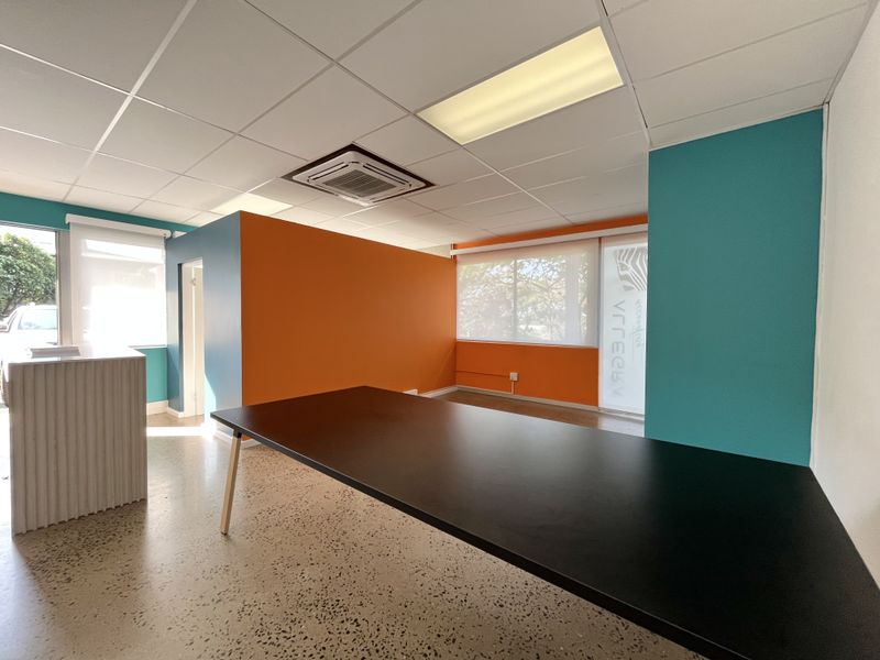 Modern office space featuring vibrant accent walls, terrazzo flooring, suspended ceiling with recessed lighting, and integrated cassette air conditioning.