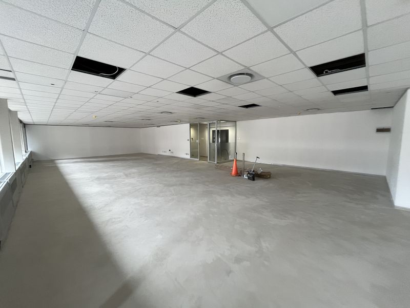 A large, open-plan office space featuring a suspended ceiling with missing tiles and unfinished flooring, ready for custom fit-out.