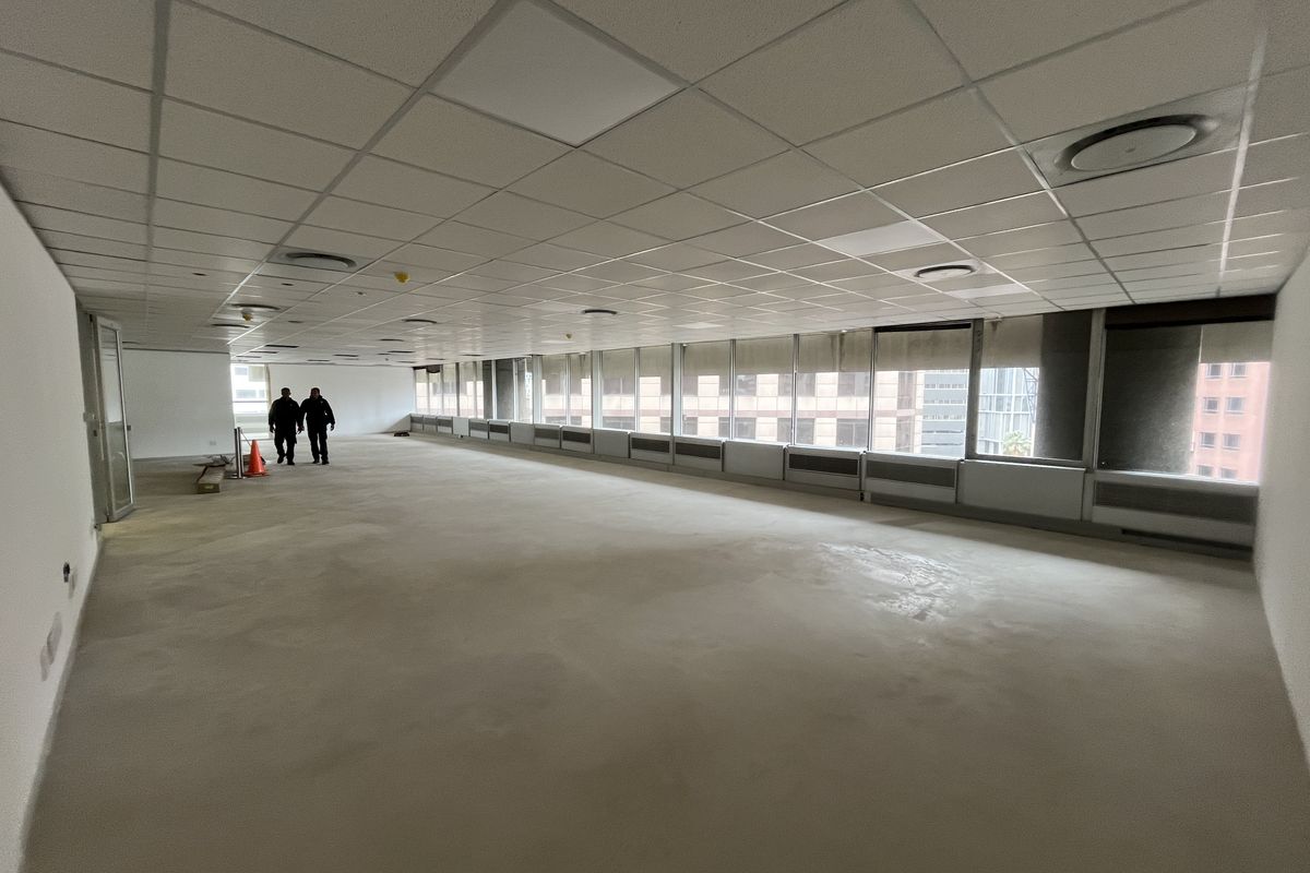 A spacious, open-plan office area featuring a suspended ceiling, recessed lighting, and large windows with blinds, offering a blank canvas for customization.