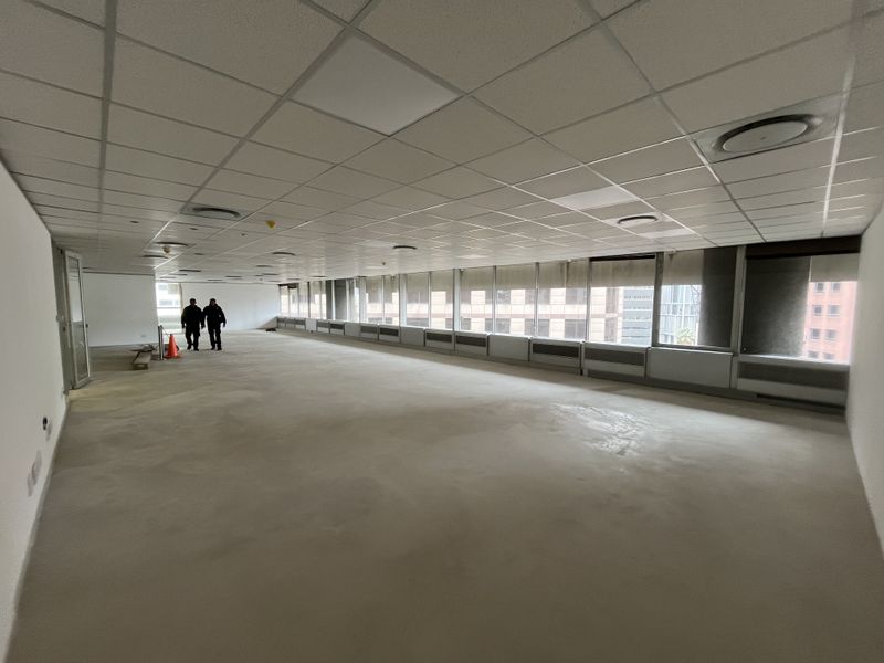 A spacious, open-plan office area featuring a suspended ceiling, recessed lighting, and large windows with blinds, offering a blank canvas for customization.