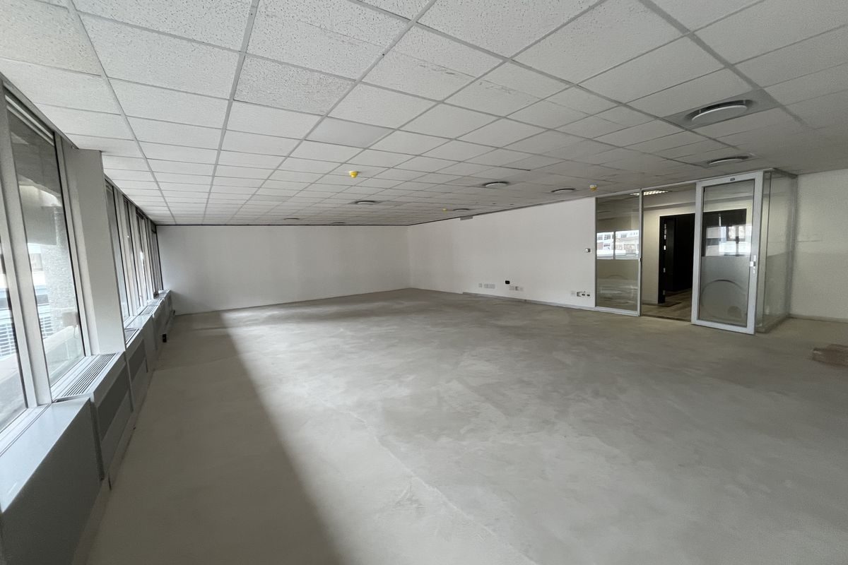 A spacious, vacant open-plan office area featuring a suspended ceiling, large windows, and a modern glass partition entrance.