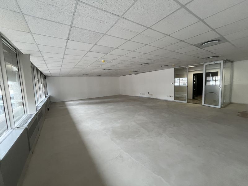 A spacious, vacant open-plan office area featuring a suspended ceiling, large windows, and a modern glass partition entrance.