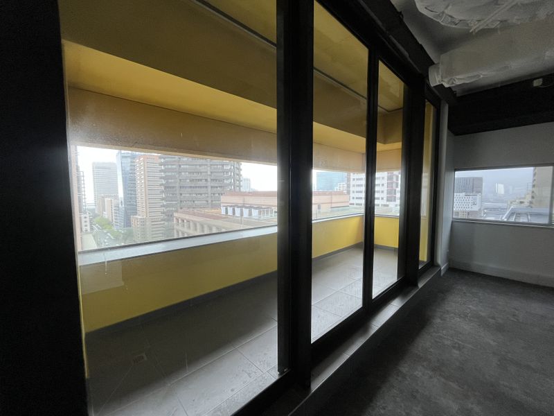 An empty balcony area featuring tiled flooring, yellow walls, and large sliding glass doors with views of the surrounding city buildings.
