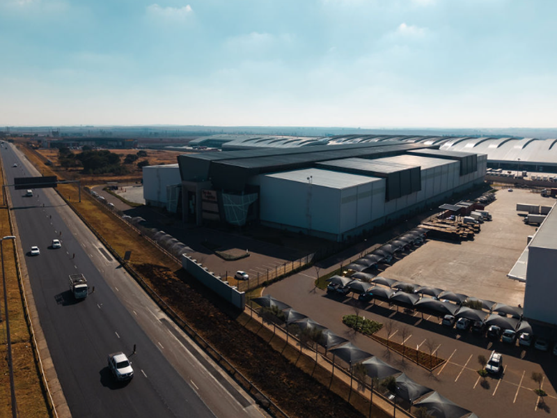 Aerial view of a large industrial warehouse facility featuring extensive paved parking, shade cloth carports, and direct access to a major highway.