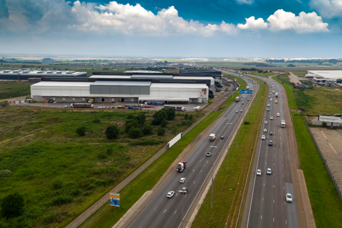 Aerial view of a large industrial warehouse facility with loading docks, situated adjacent to a major highway for excellent logistics and transport access.