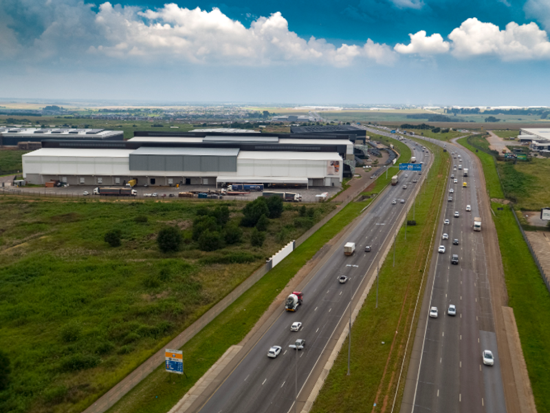 Aerial view of a large industrial warehouse facility with loading docks, situated adjacent to a major highway for excellent logistics and transport access.